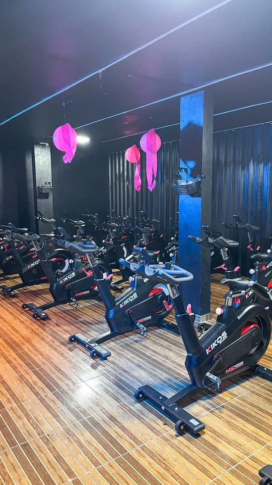 Fileiras de bikes indoor na sala de bike da Performance, com luz neon azul e balões rosa